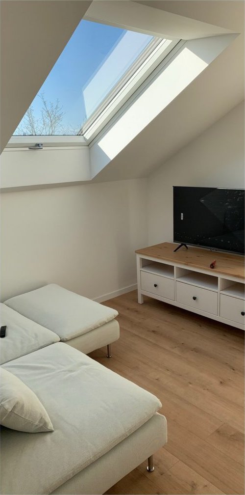 Fertig ausgebauter Wohnraum unter dem Dach mit Dachfenster, hellem Sofa und Holzboden